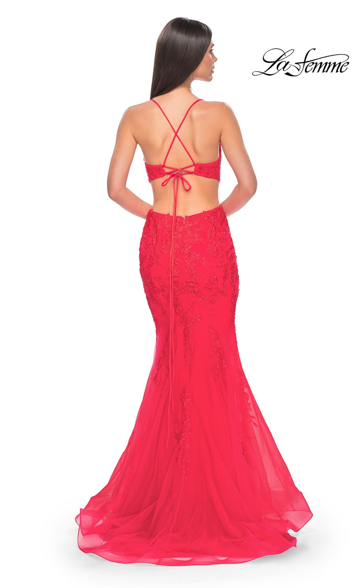 A woman with long brown hair showcases the La Femme Long Lace Mermaid Prom Dress 31133, a floor-length bright red gown with lace detailing and crisscross back straps, shown from the back.